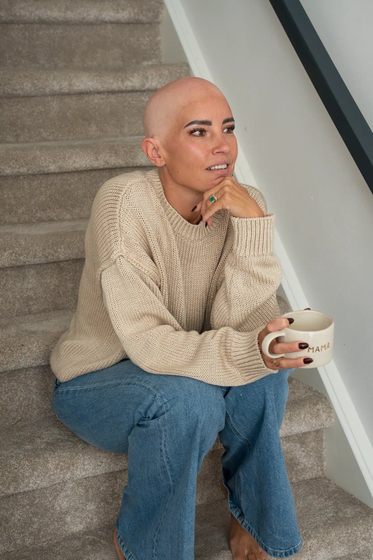 Natalie, She Is Wearing It founder with alopecia, sitting thoughtfully on the stairs with a mug